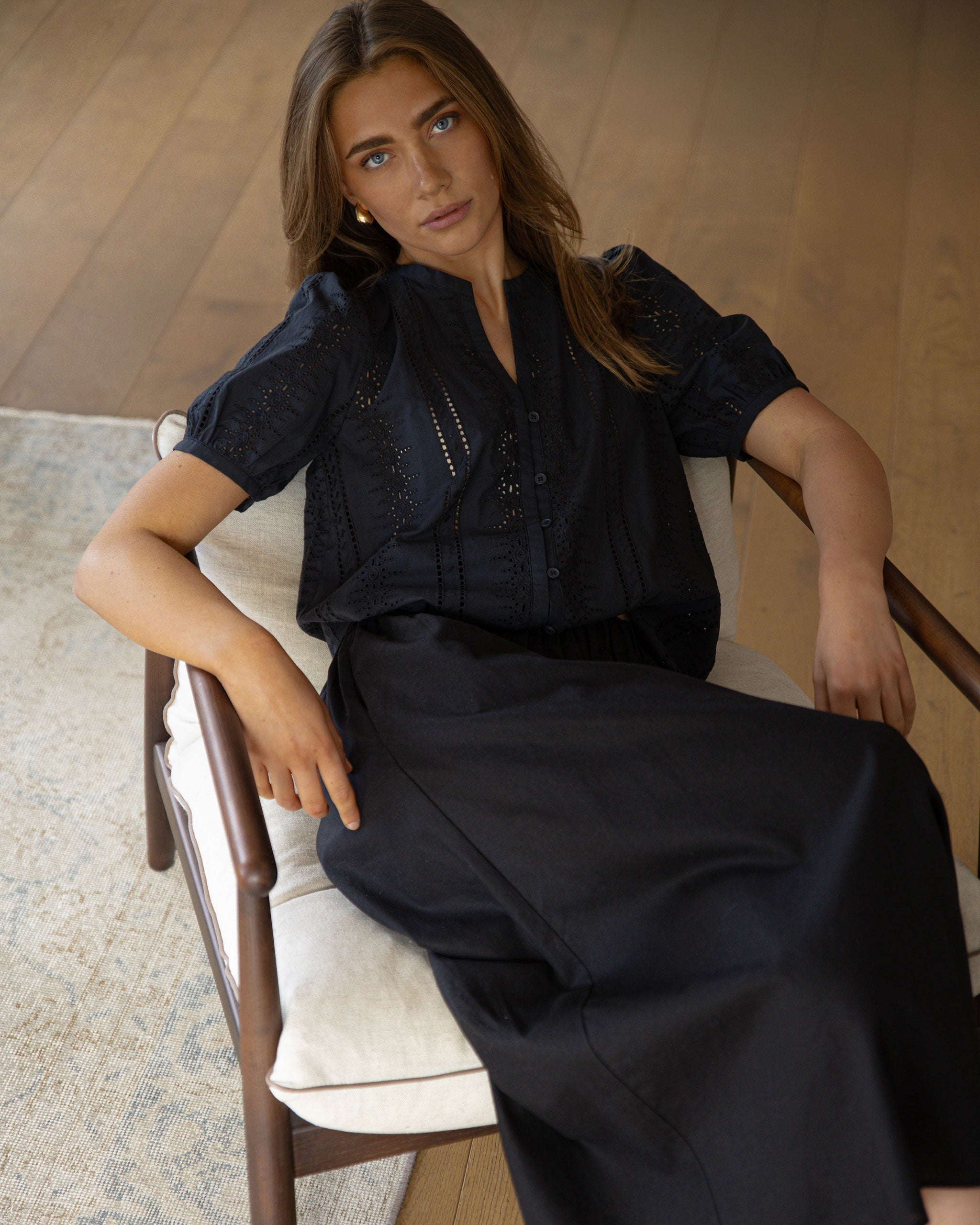 Woman sitting on a chair wearing a black outfit with a neutral background