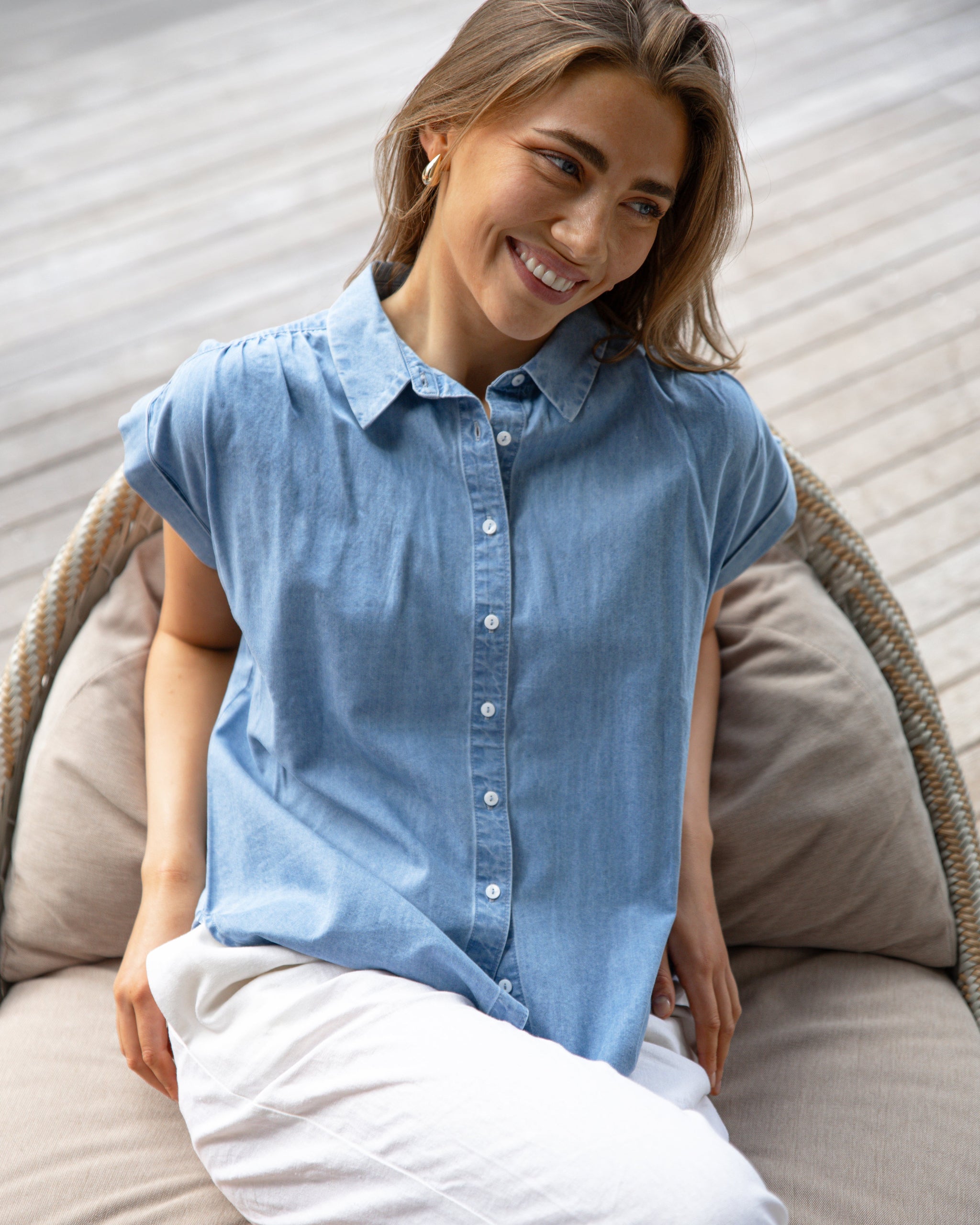Woman wearing a blue denim shirt sitting on a beige cushioned chair.
