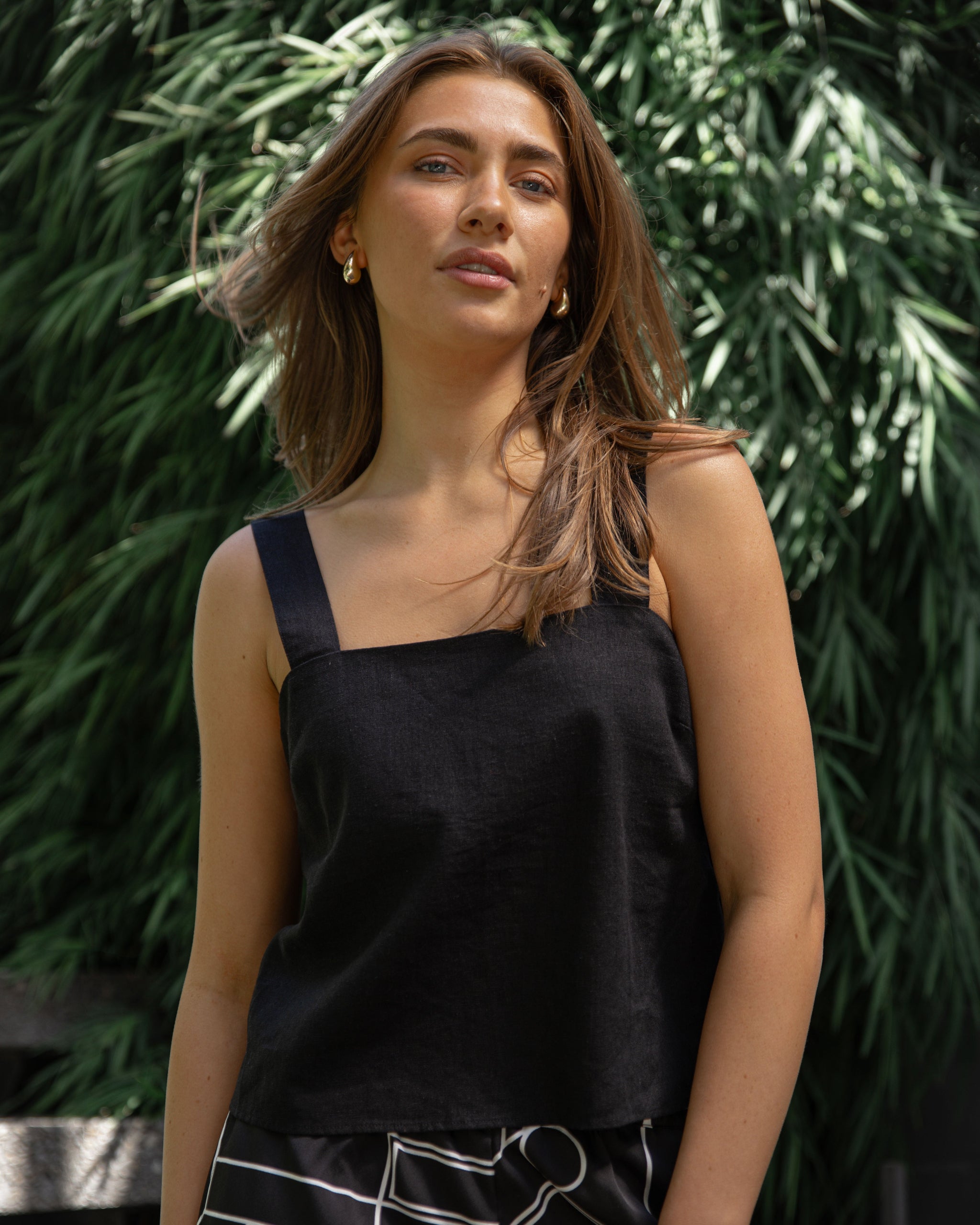 Woman wearing a black sleeveless top with a green leafy background