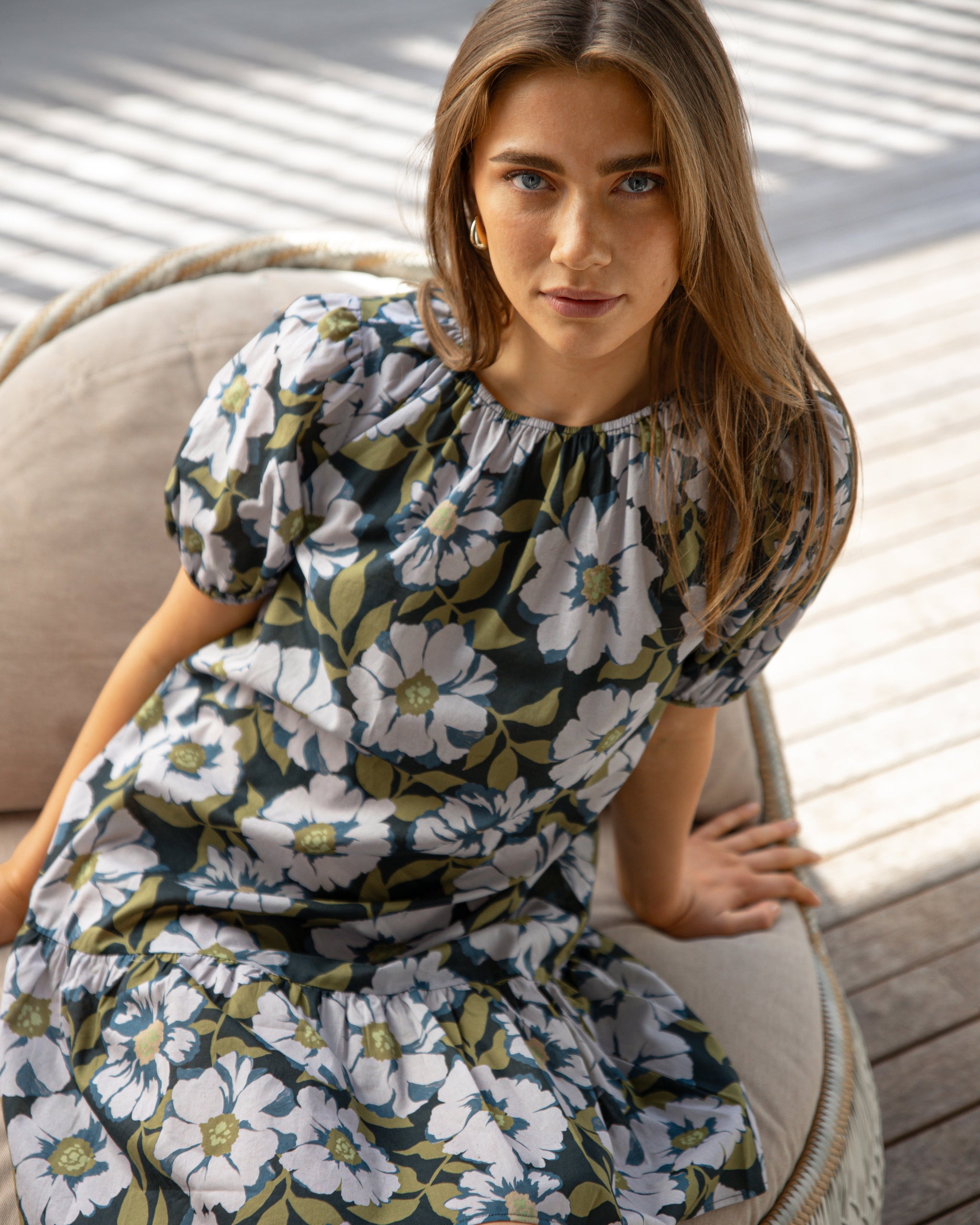 Woman wearing a floral dress sitting on a chair outdoors.