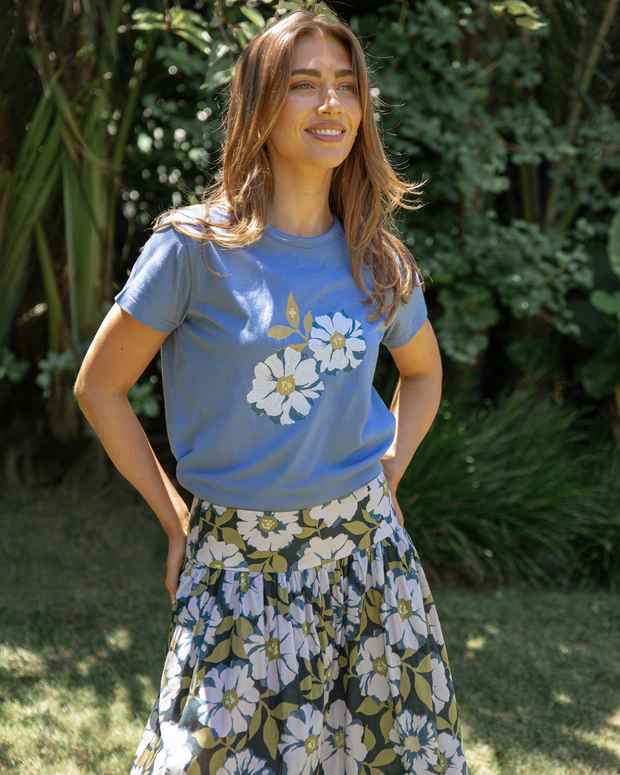 Woman wearing a blue t-shirt with floral design and a floral skirt outdoors.