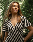 Woman wearing a black and white striped dress standing in a tropical setting.