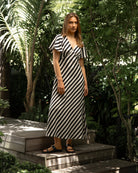 Woman in a black and white striped dress standing on wooden steps with greenery around.