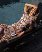 Woman in a colorful quilted dress lying on a lounge chair by a pool.